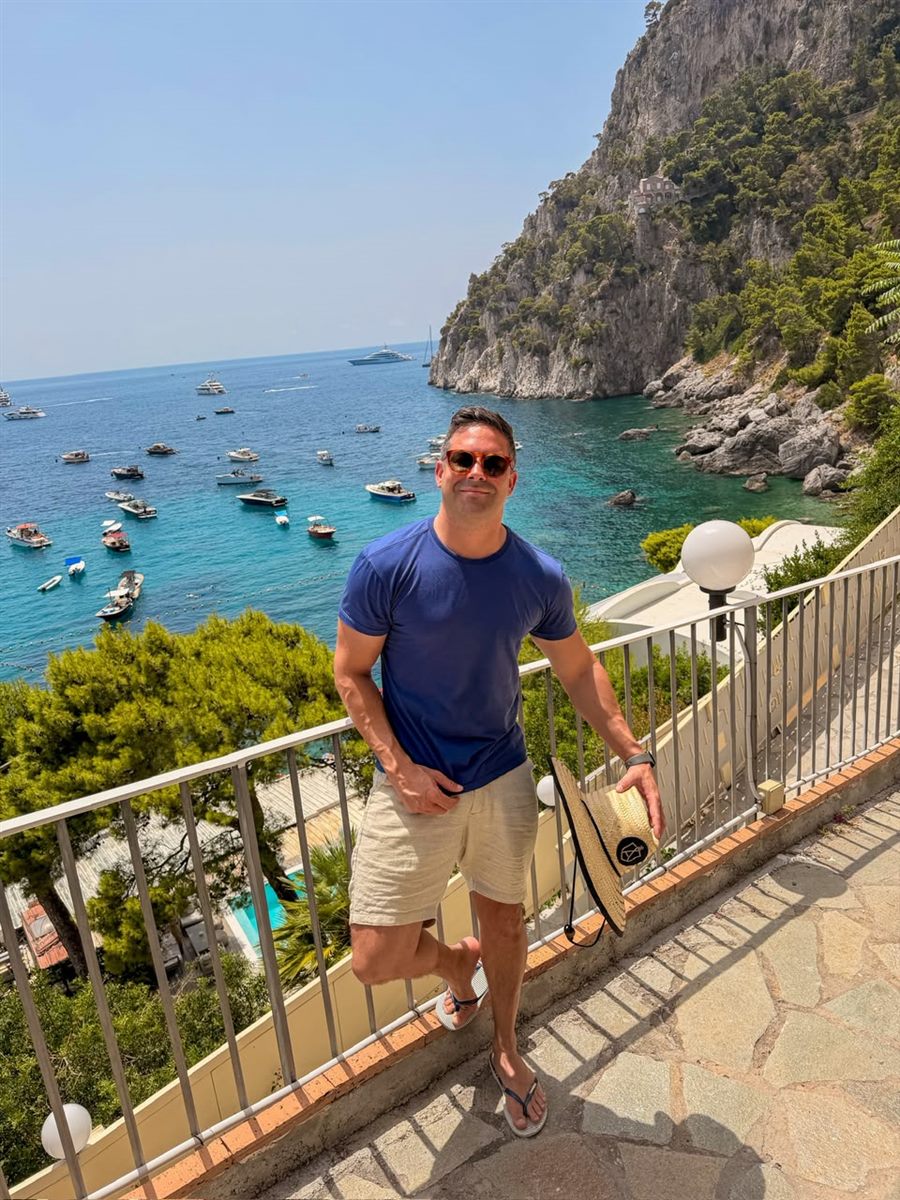 Alê Silveira em Capri, com a costa e as embarcações ao fundo
